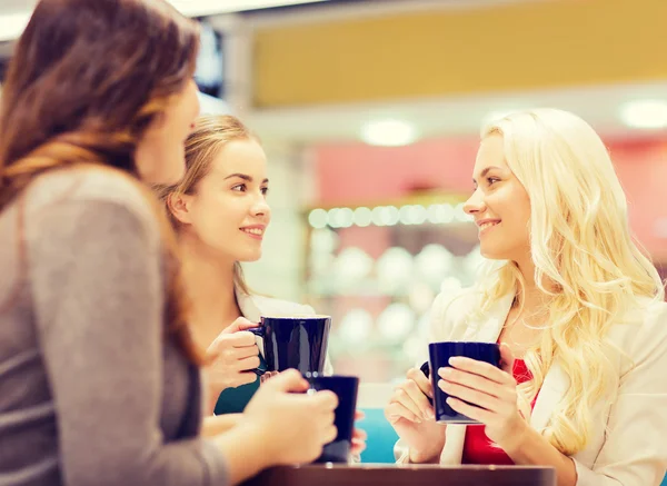 Mujeres jóvenes sonrientes con tazas en el centro comercial o cafetería —  Fotos de Stock