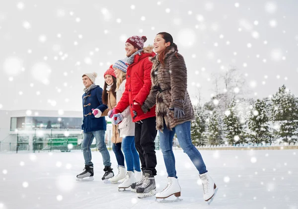 Amigos felices patinaje sobre hielo en pista al aire libre — Foto de Stock