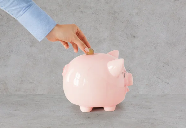 Fechar a mão colocando moeda para o banco porquinho — Fotografia de Stock