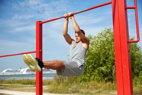 Joven ejercitándose en barra horizontal al aire libre — Foto de Stock