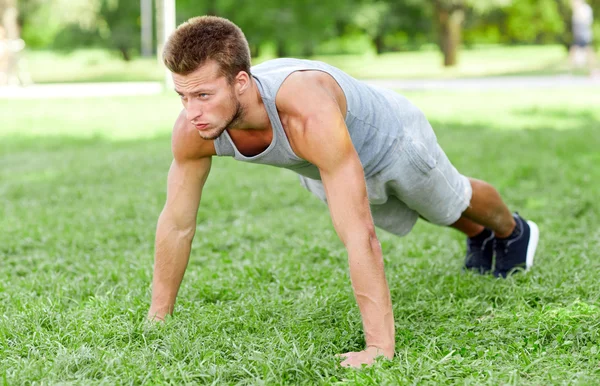 Young man doing push ups on grass in summer park — Stock Photo, Image