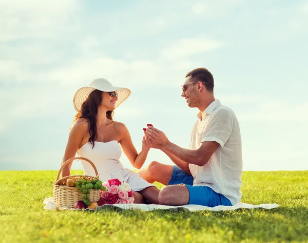 Sonriente pareja con pequeña caja de regalo roja en el picnic —  Fotos de Stock