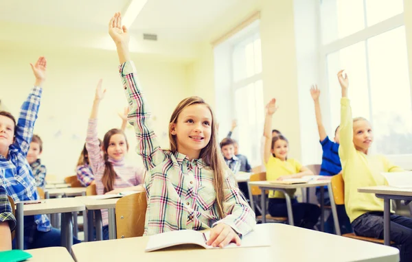 group of school kids raising hands in classroom