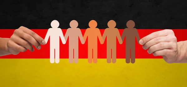 Mãos com papel pessoas pictograma sobre bandeira alemã — Fotografia de Stock