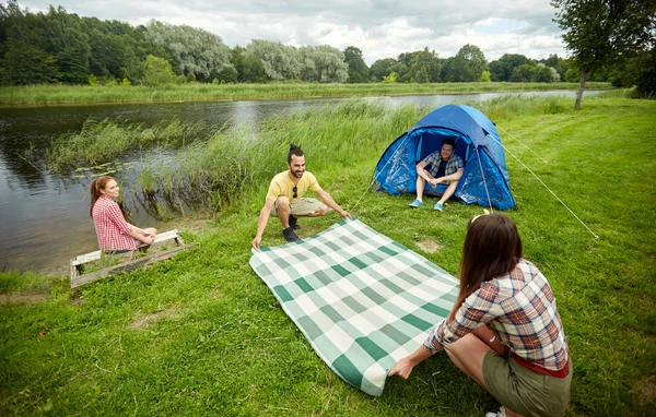 Happy friends laying picnic blanket at campsite — 图库照片