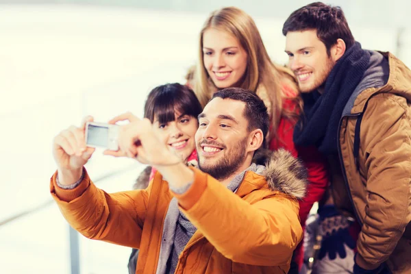 Happy friends with camera on skating rink — Stock Photo, Image