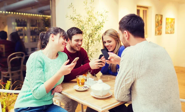 Группа друзей со смартфонами, встречающихся в кафе — стоковое фото