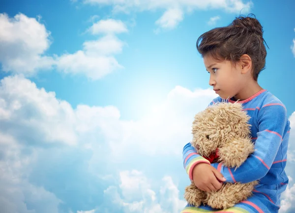 Sad little girl with teddy bear toy over blue sky — Stock Photo, Image