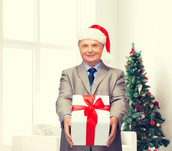 Uomo sorridente in abito e cappello da Babbo Natale con regalo — Foto Stock