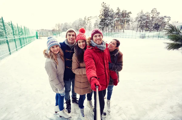 Amigos felizes com smartphone na pista de patinação no gelo — Fotografia de Stock