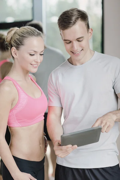 Smiling young woman with personal trainer in gym — Stock Photo, Image