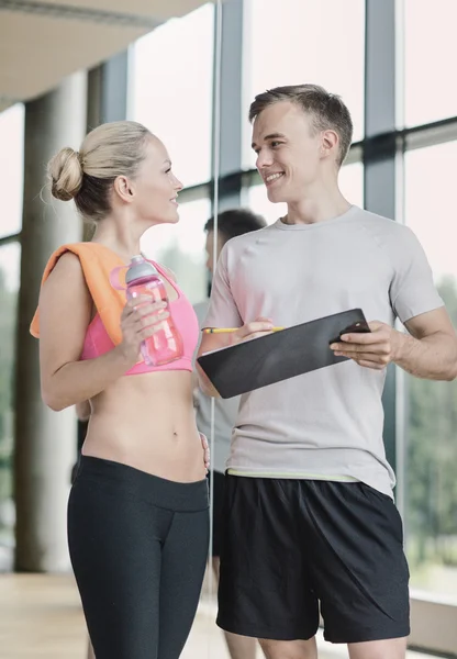 Giovane donna sorridente con personal trainer in palestra — Foto Stock