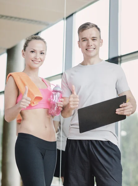 Spor salonunda kişisel antrenörüyle gülümseyen genç bir kadın. — Stok fotoğraf