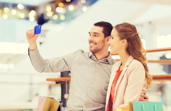 Happy couple with smartphone taking selfie in mall — Stock Photo, Image