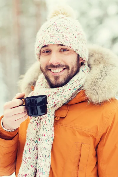 Улыбающийся молодой человек с чашей в зимнем лесу — стоковое фото