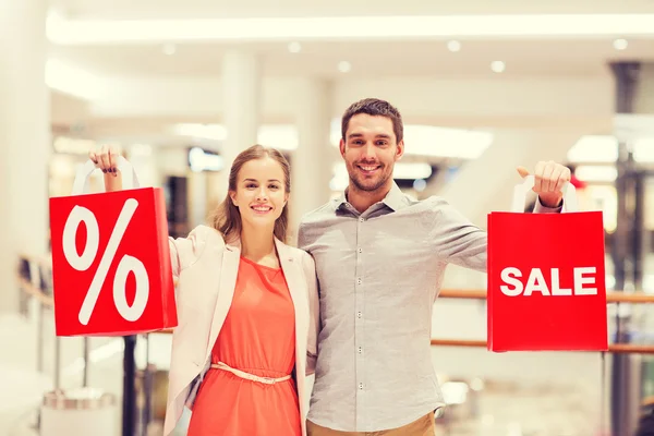 Happy young couple with red shopping bags in mall — Stock Photo, Image