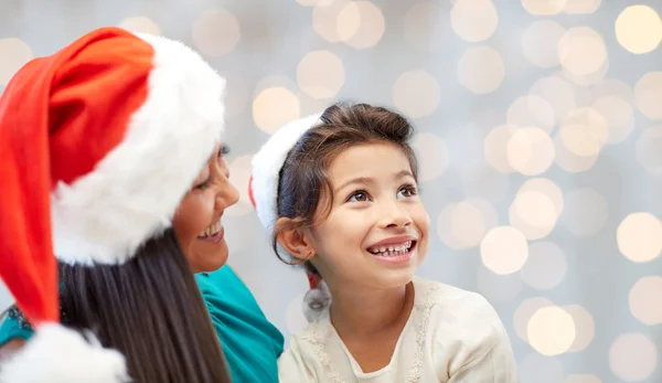 Gelukkig moeder en meisje in santa hoeden thuis — Stockfoto