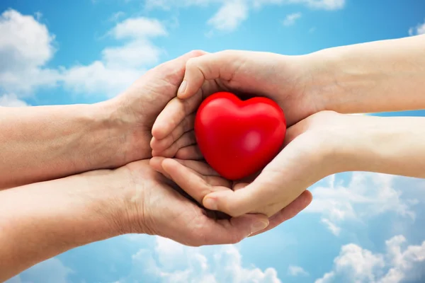 Seniores e jovens mãos de mulher segurando coração vermelho Imagem De Stock