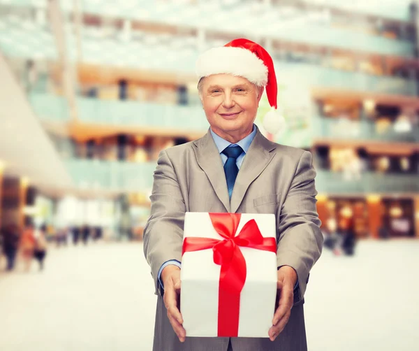 Hombre sonriente en traje y sombrero de ayudante de santa con regalo —  Fotos de Stock