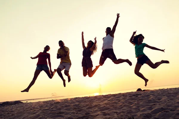 Lachende vrienden dansen en springen op strand — Stockfoto