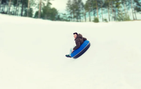 Heureux jeune homme glissant vers le bas sur la neige tube — Photo