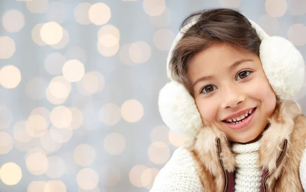 Happy little girl in earmuffs over holidays lights — Stock Photo, Image