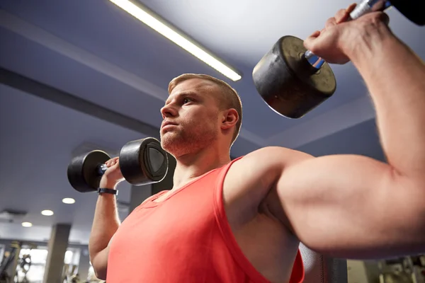 Jeune homme avec haltères flexion des muscles dans la salle de gym — Photo