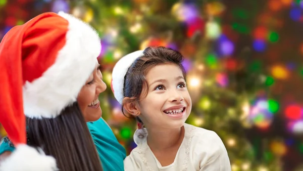 Gelukkig moeder en meisje in santa hoeden thuis — Stockfoto