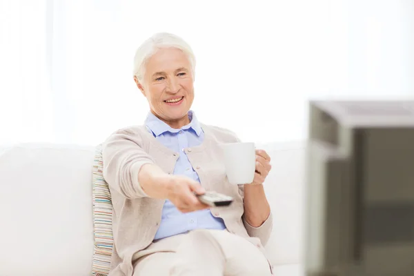 Пожилая женщина смотрит телевизор и пьет чай дома — стоковое фото