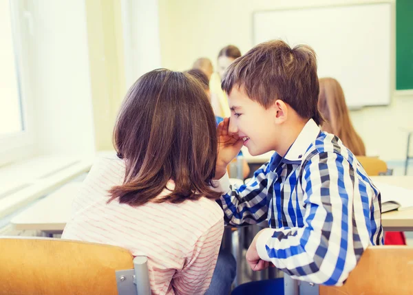 Glimlachend schoolmeisje aan klasgenoot oor fluisteren — Stockfoto