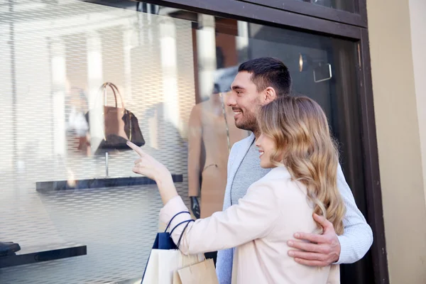 Happy couple with shopping bags at shop window — Stock Photo, Image