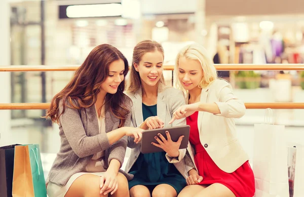 Mulheres jovens felizes com tablet pc e sacos de compras — Fotografia de Stock