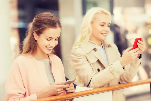 Mulheres felizes com smartphones e sacos de compras — Fotografia de Stock