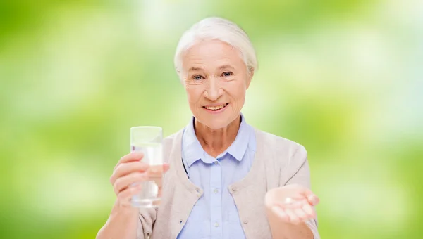 Happy senior woman with water and medicine — Stock Photo, Image