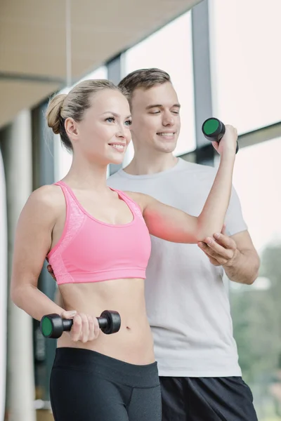 Smiling young woman with personal trainer in gym — Stock Photo, Image