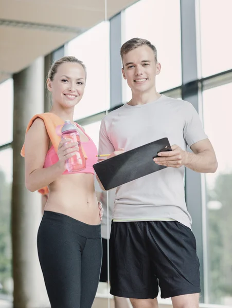 Smiling young woman with personal trainer in gym — Stock Photo, Image