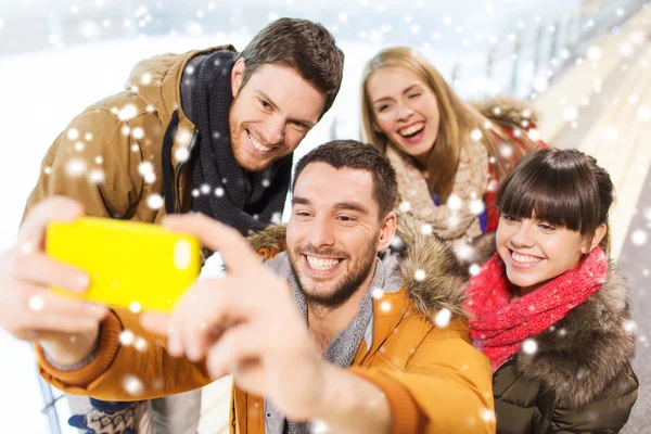 Happy friends with smartphone on skating rink — Stock Photo, Image
