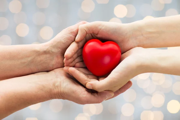 Seniores e jovens mãos de mulher segurando coração vermelho — Fotografia de Stock