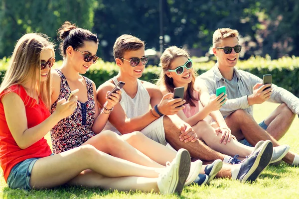 Amigos sonrientes con teléfonos inteligentes sentados en la hierba — Foto de Stock