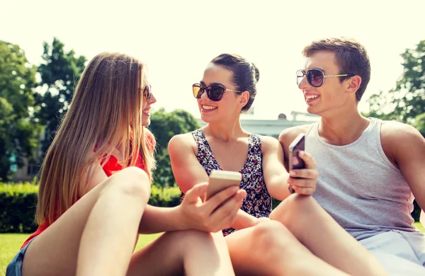 Lächelnde Freunde mit Smartphones im Gras — Stockfoto