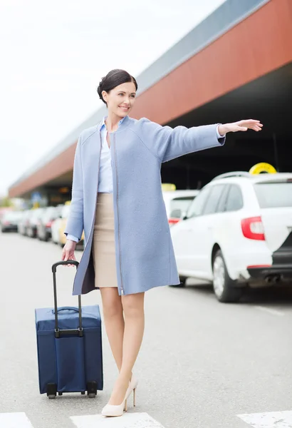 Smiling young woman with travel bag catching taxi — Stock Photo, Image