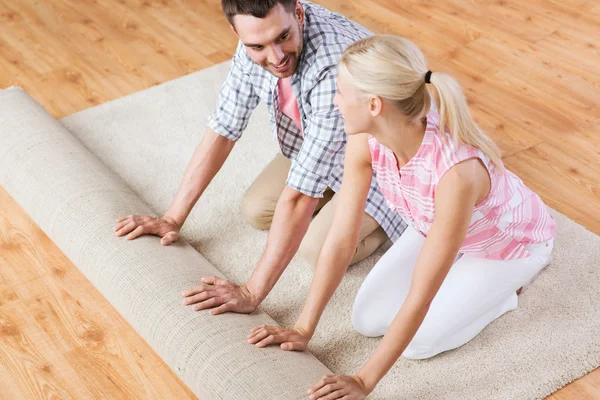 Feliz pareja desenrollando alfombra o alfombra en casa —  Fotos de Stock