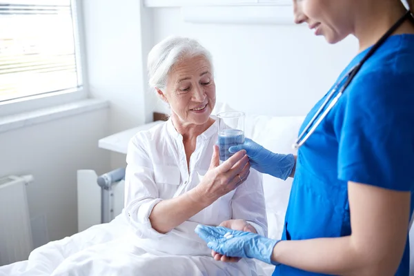 Nurse giving medicine to senior woman at hospital — Stock Photo, Image