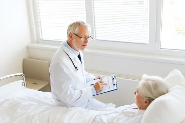 Seniorin und Arzt mit Klemmbrett im Krankenhaus — Stockfoto