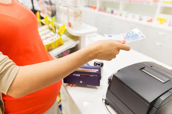 Gravid kvinna med pengar i kassan i apotek — Stockfoto
