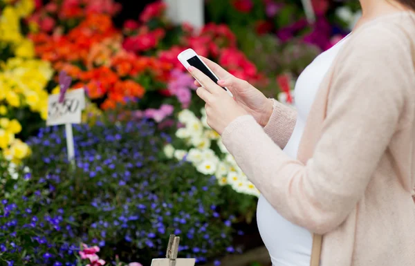 Mulher grávida com smartphone no mercado de flores — Fotografia de Stock