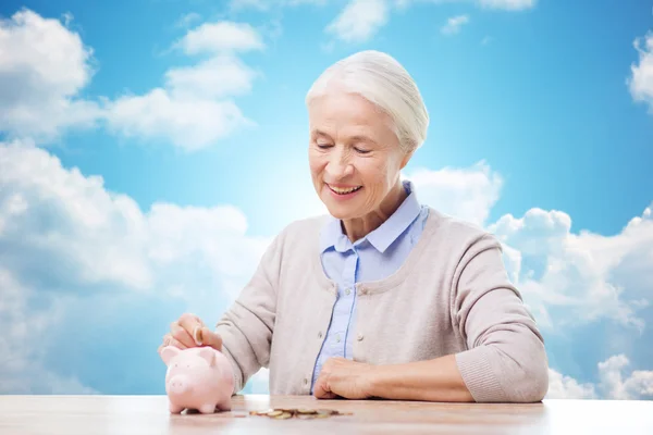 Sênior mulher colocando dinheiro para porquinho banco — Fotografia de Stock