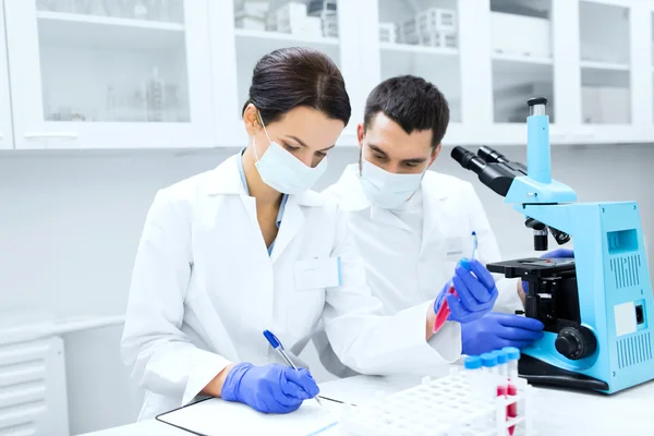 Científicos con portapapeles y microscopio en laboratorio — Foto de Stock