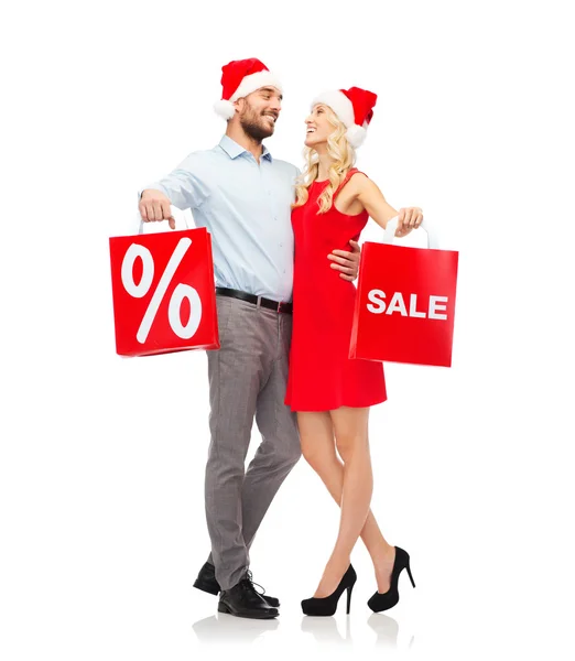 Feliz pareja en sombreros de santa con bolsas de compras rojas — Foto de Stock