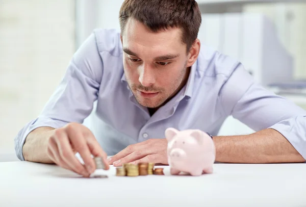 Homem de negócios com banco porquinho e moedas no escritório — Fotografia de Stock